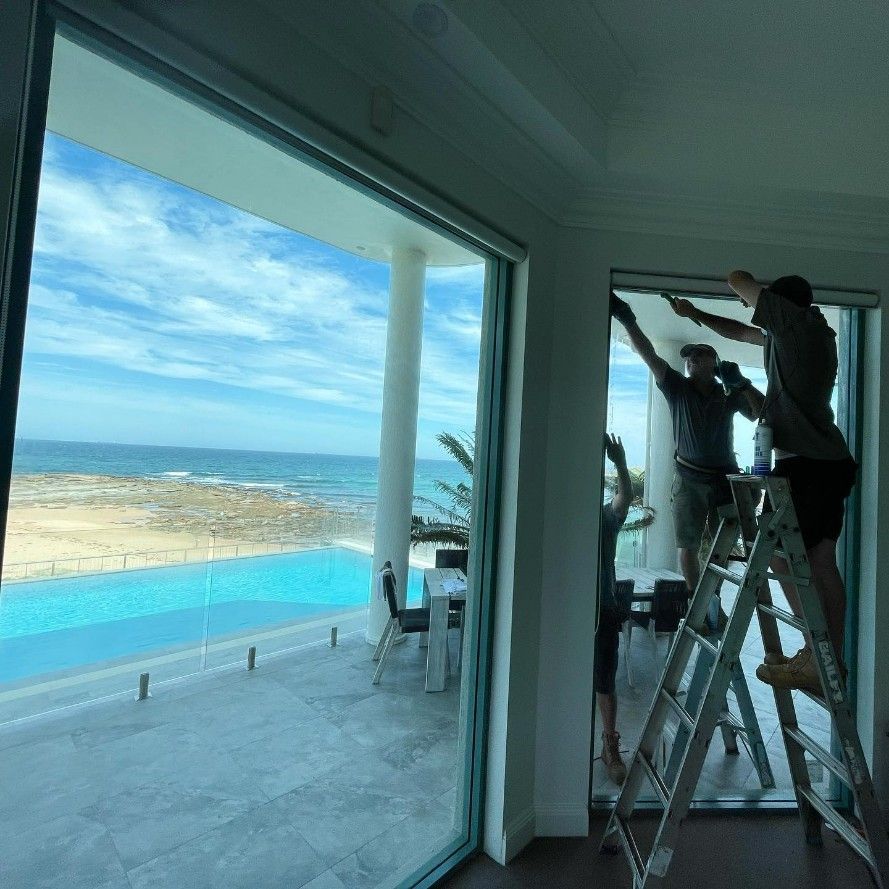 Workers installing large windows in a coastal home overlooking the ocean and pool.
