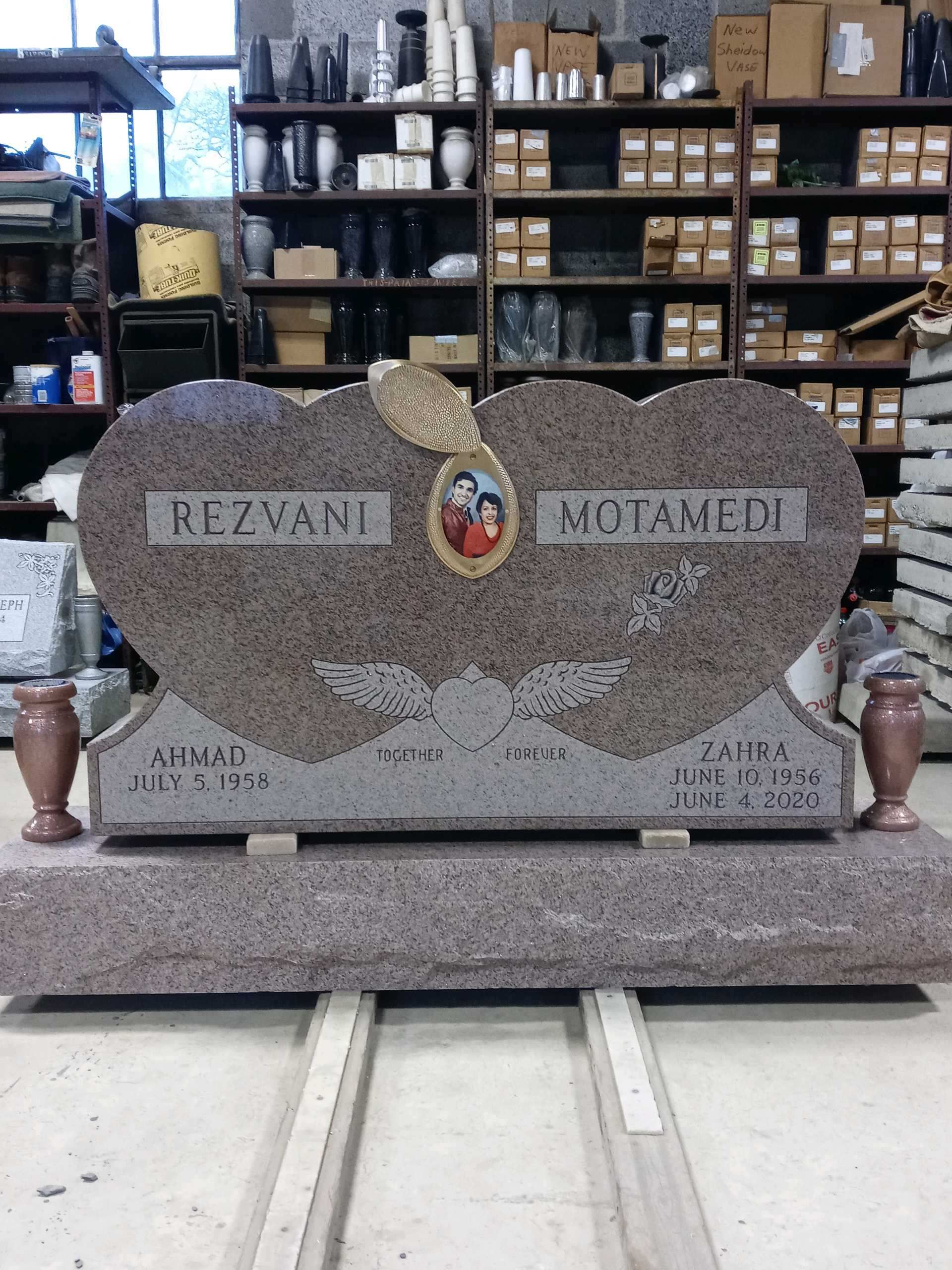 A double heart-shaped granite headstone, engraved with names and a portrait, in a workshop.