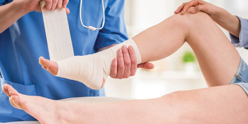 A doctor is bandaging a patient 's ankle.