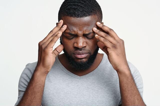 A man with a beard is holding his head in pain.