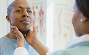 A woman is examining a man 's neck in front of a mirror.