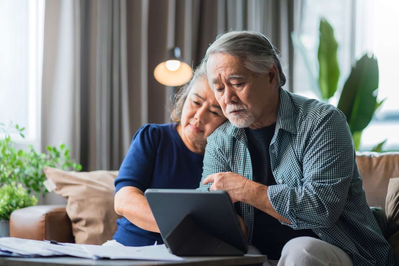 Two people reviewing a tablet together on a couch in a bright living room