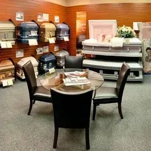 Funeral home showroom with caskets, floral arrangement, and a small table with chairs