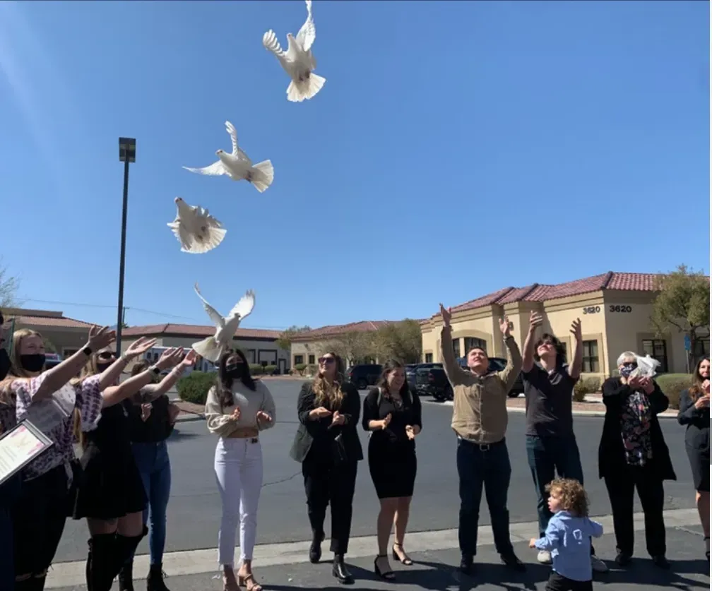 People releasing white doves into a sunny sky outside a building