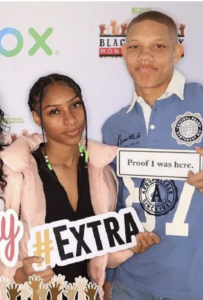 Two people posing with “#EXTRA” and “Proof I was here” signs at an event backdrop