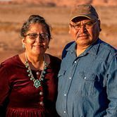 Smiling couple standing outdoors in warm sunset light, with a blurred desert landscape behind them