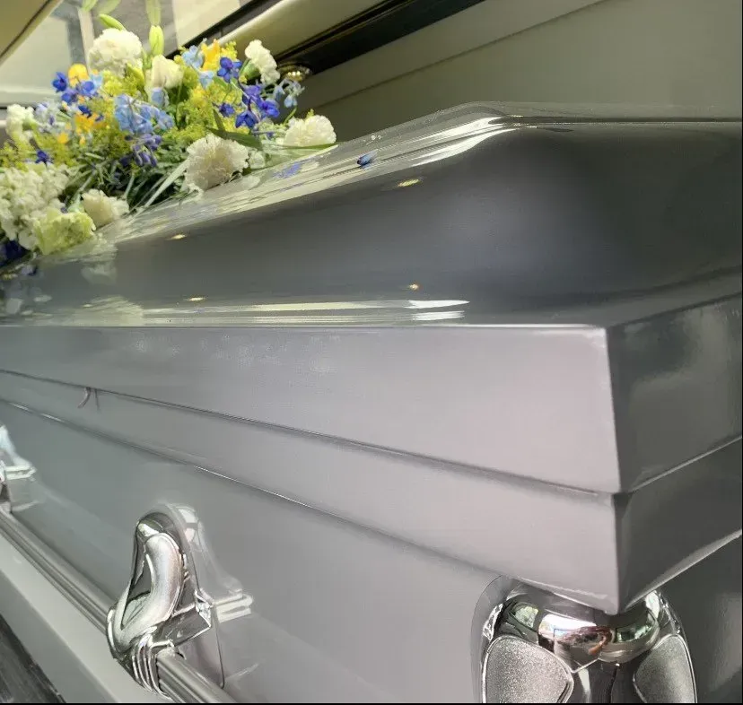 Silver casket with white and blue flowers on top in a funeral setting