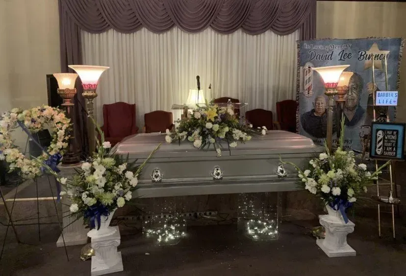Silver casket surrounded by white floral arrangements at a memorial service setup