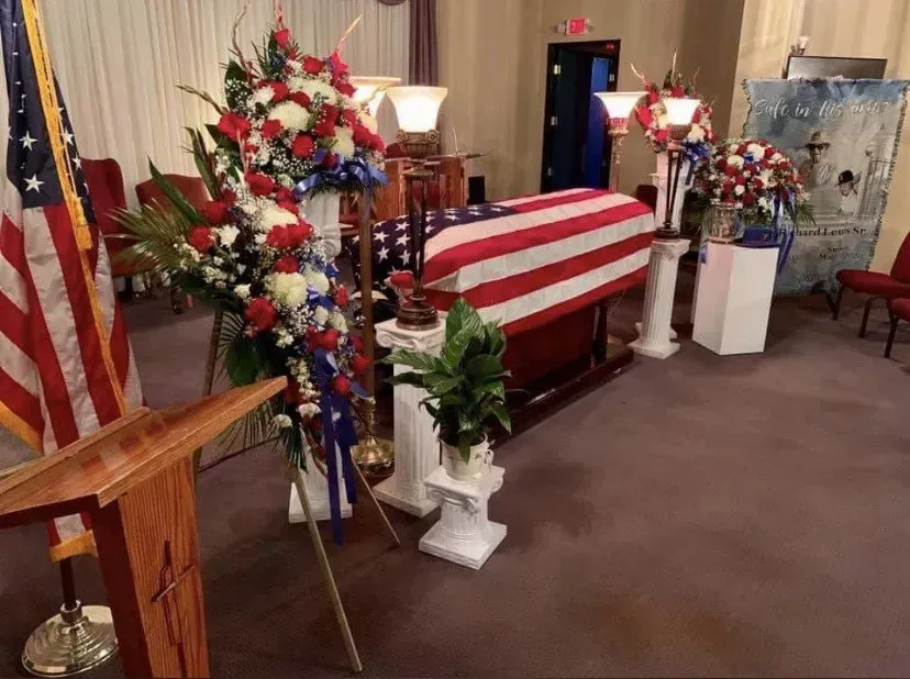 American flag-draped casket with red, white, and blue floral arrangements in a memorial room