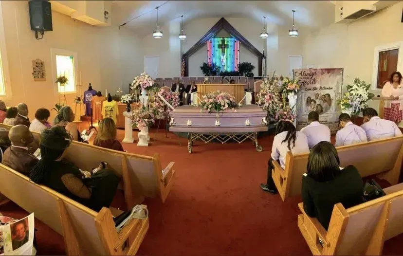 Funeral service in a church, with a casket at the front and mourners seated in pews.