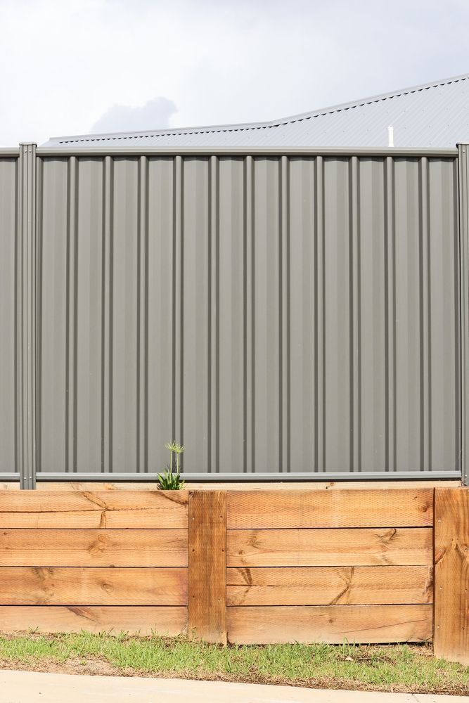 Gray Corrugated Metal Fence Above a Wooden Retaining Wall — Fencing Around in Garbutt, QLD