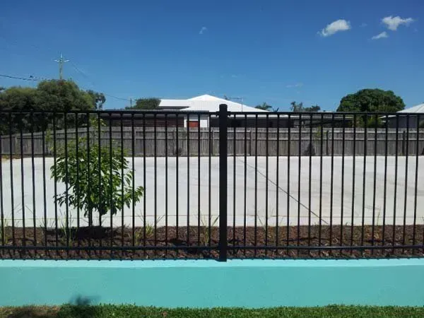 Black Metal Fence Beside a Turquoise Wall, With a Small Tree and Open Paved Lot — Fencing Around in Garbutt, QLD
