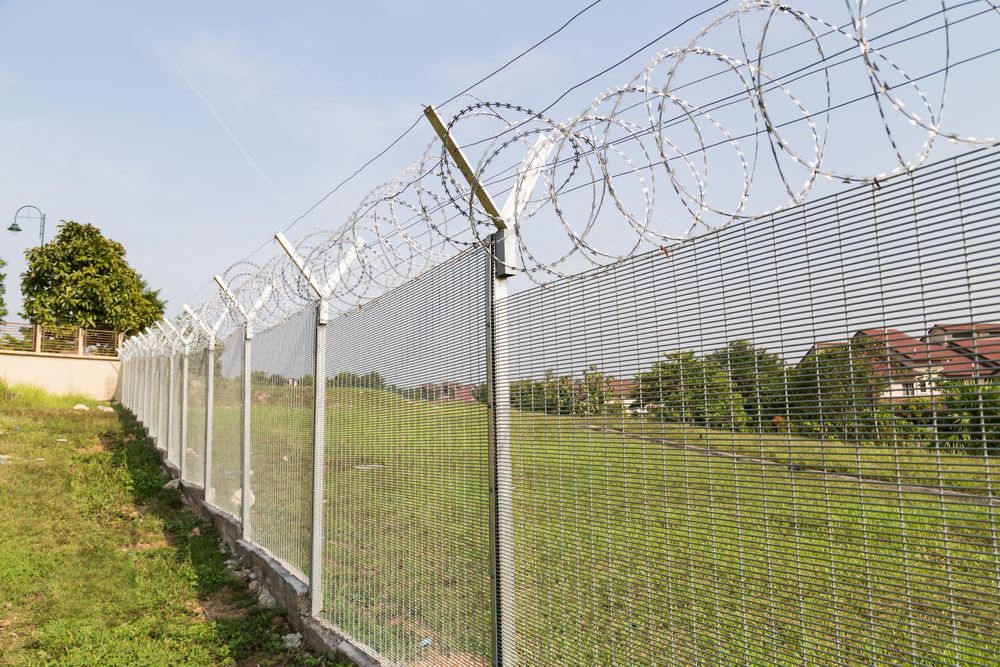 Tall Chain-link Fence Topped With Barbed Wire Bordering a Grassy Field Under a Blue Sky — Fencing Around in Garbutt, QLD