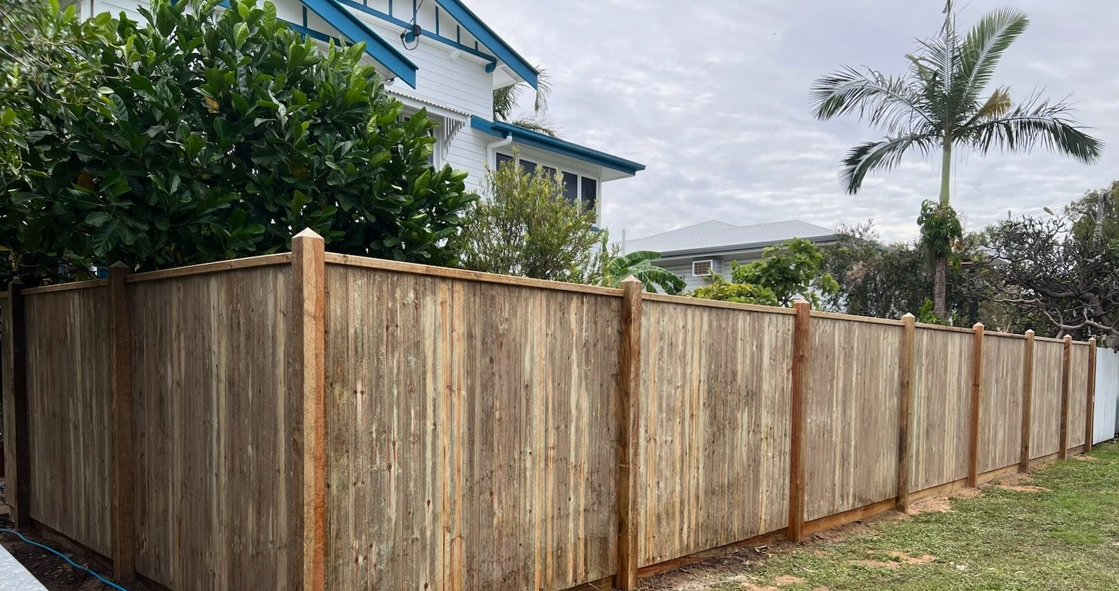 Wooden Privacy Fence Along a Grassy Yard Beside a House and Palm Tree — Fencing Around in Garbutt, QLD