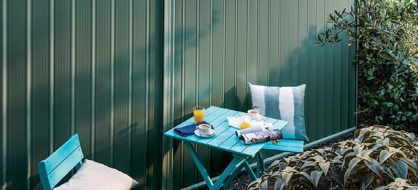 Small Blue Patio Table Set on a Green Deck Beside a Fence and Plants — Fencing Around in Garbutt, QLD