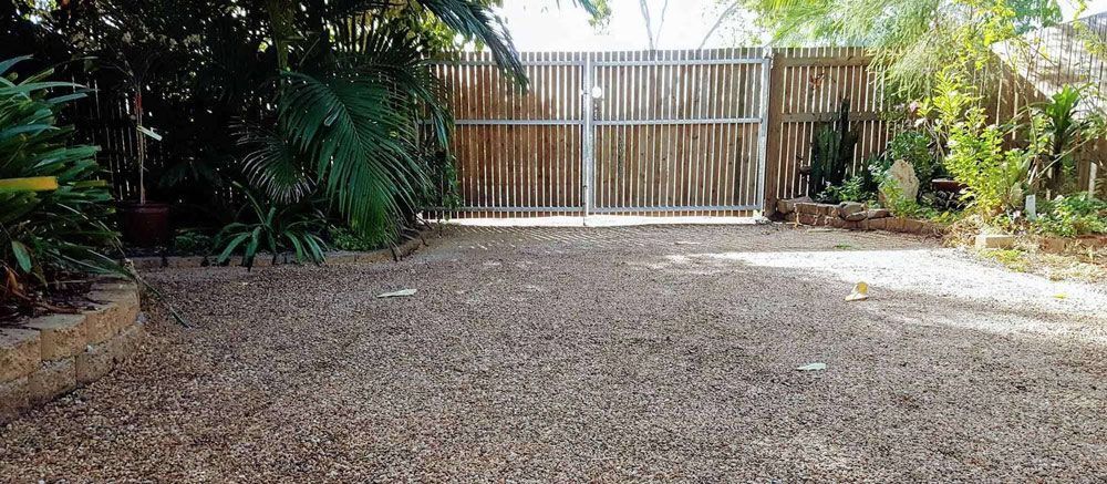 Gravel Driveway Leading to a Closed Wooden Gate, Framed by Lush Green Plants on Both Sides — Fencing Around in Garbutt, QLD