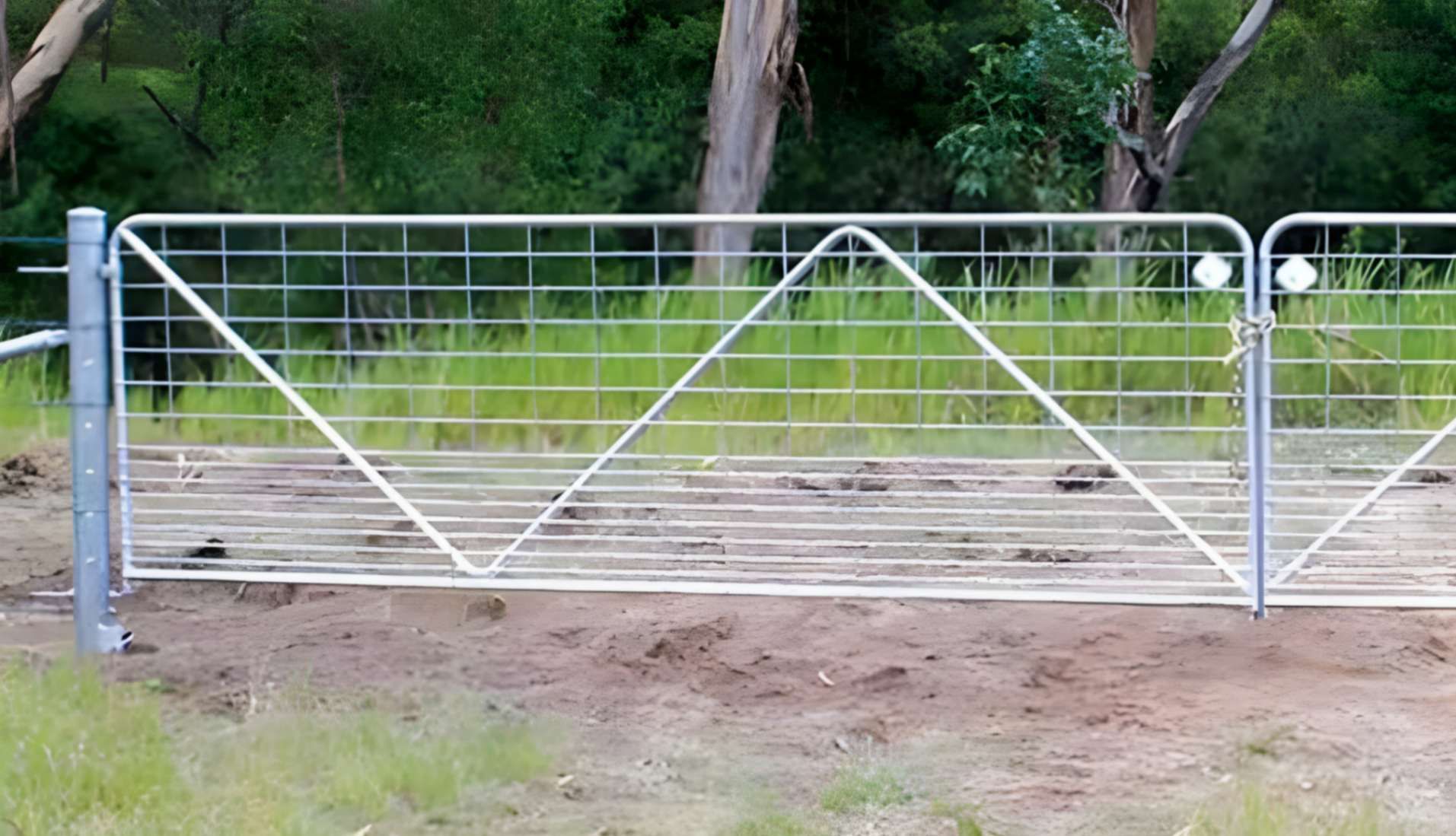 White Metal Farm Gate With Diagonal Support Bars Beside a Dirt Driveway and Green Grass — Fencing Around in Garbutt, QLD