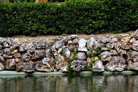 Stone Retaining Wall Beside Calm Water, Topped With Dense Green Hedges — Fencing Around in Garbutt, QLD