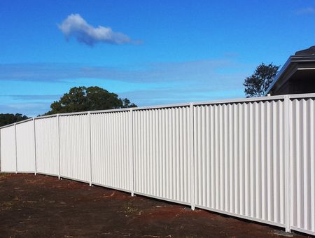 White Corrugated Fence Curving Along a Dirt Yard Under a Bright Blue Sky With Clouds — Fencing Around in Garbutt, QLD