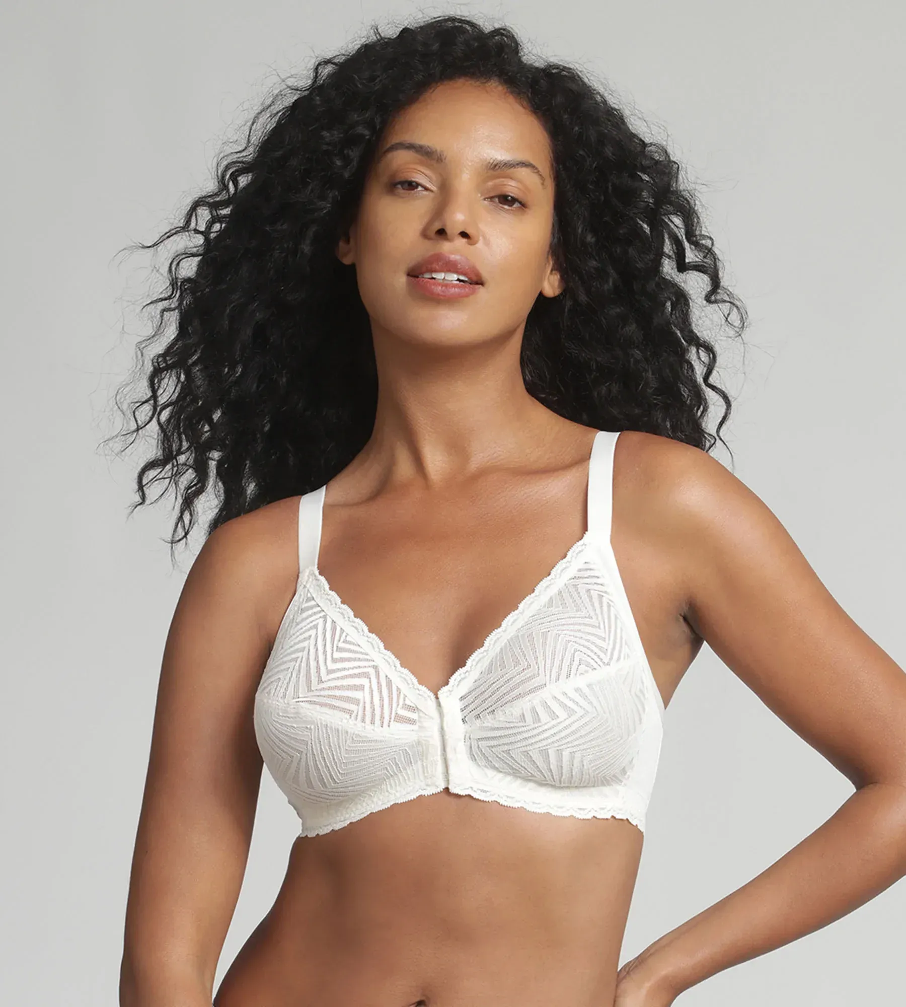 Una persona indossa un reggiseno di pizzo testurizzato bianco, con chiusura frontale e spalline larghe, su uno sfondo grigio chiaro.