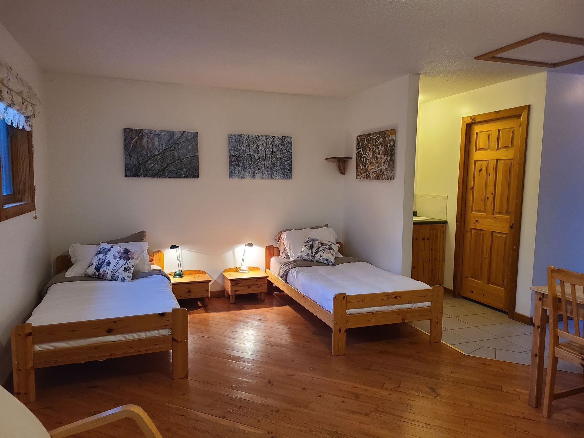 Two twin beds in a room with wood flooring and artwork. A wooden door is partially visible.