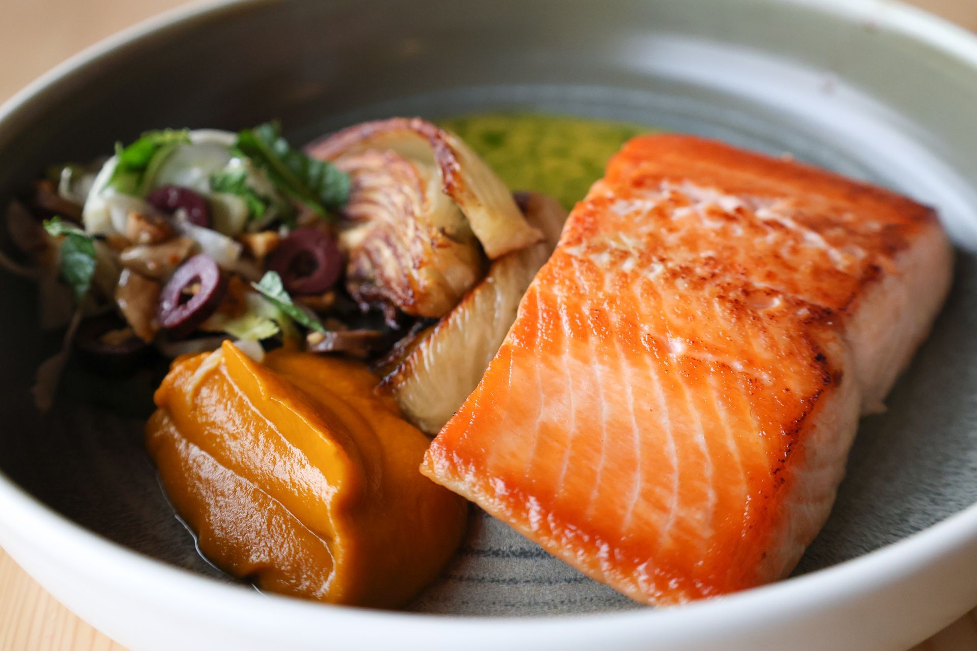 Pan-seared salmon fillet with sides of mashed squash, roasted vegetables, and pesto.