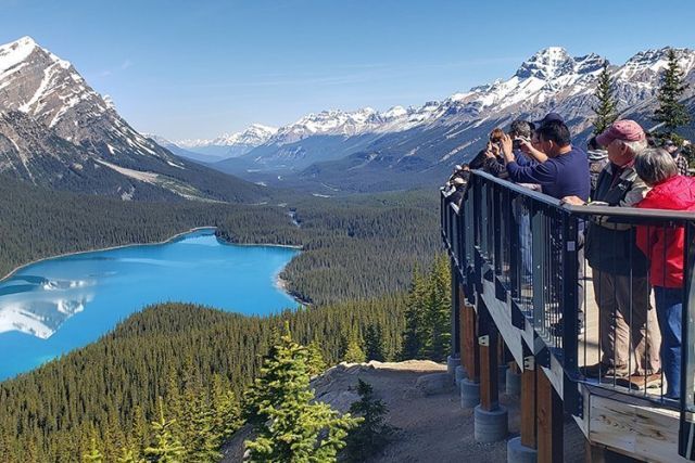 People looking at turquoise lake and mountains from a viewing platform.