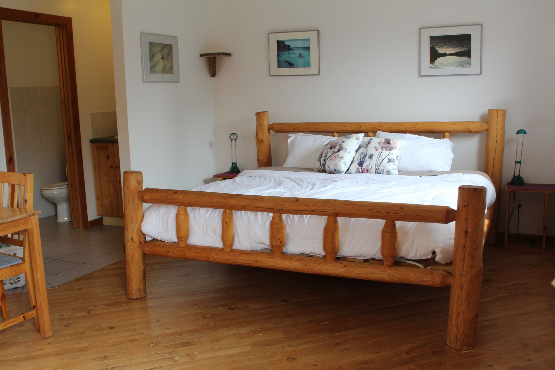 Bedroom with wooden bed frame, white bedding, and framed artwork on the wall.