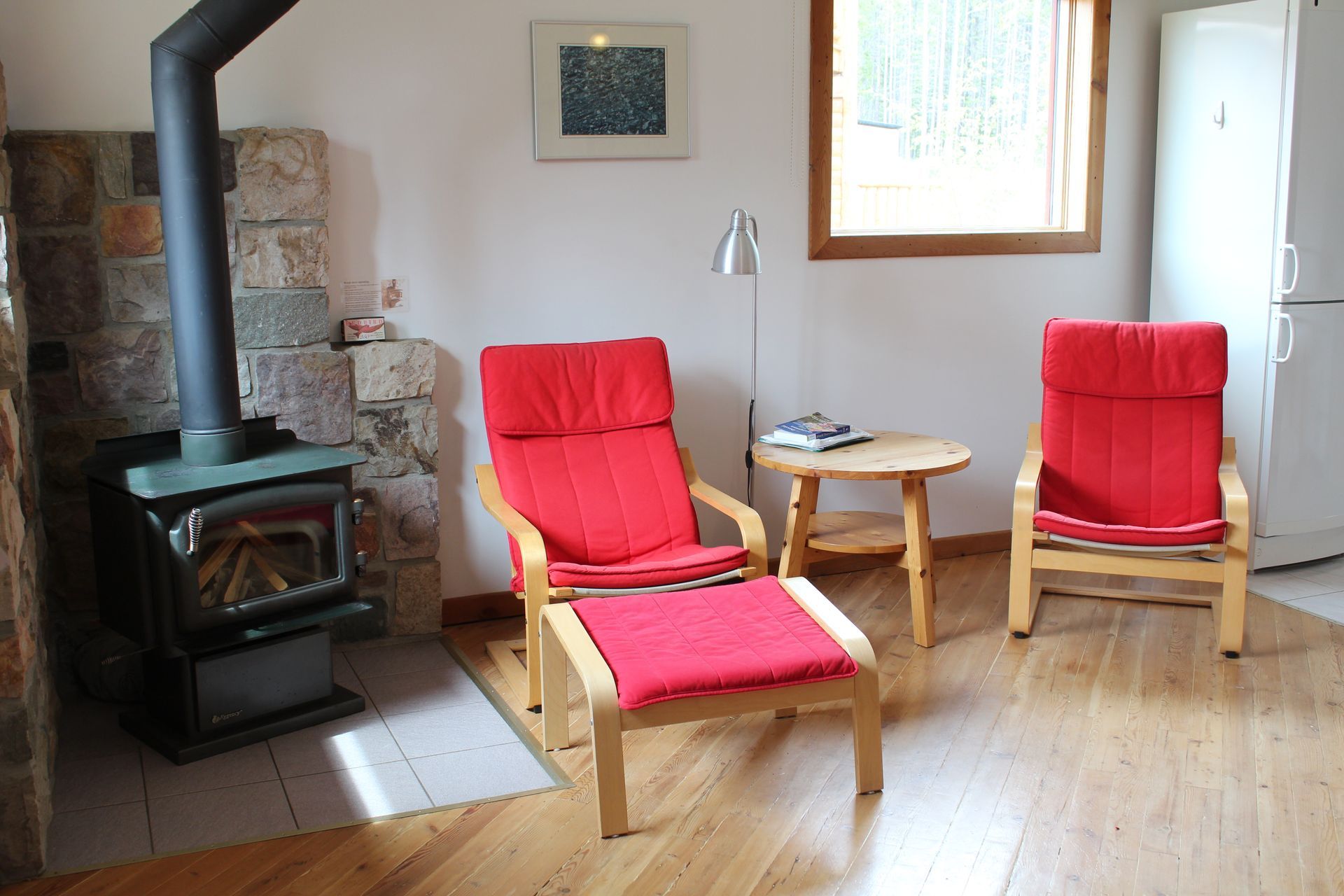 Cozy living room with red chairs, a wood stove, small table, and a window.