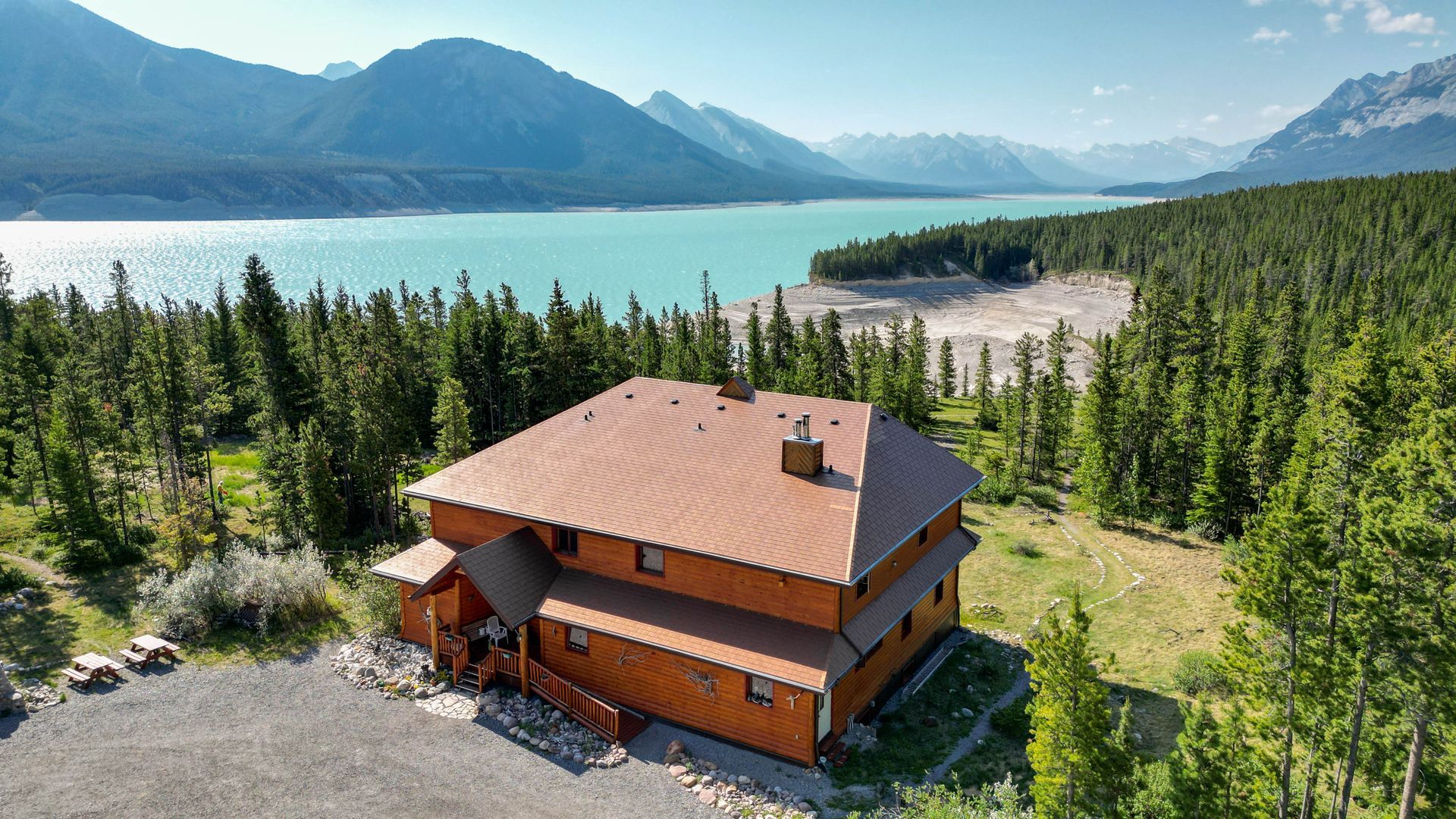 Wooden lodge overlooking a turquoise lake surrounded by mountains and a forest.