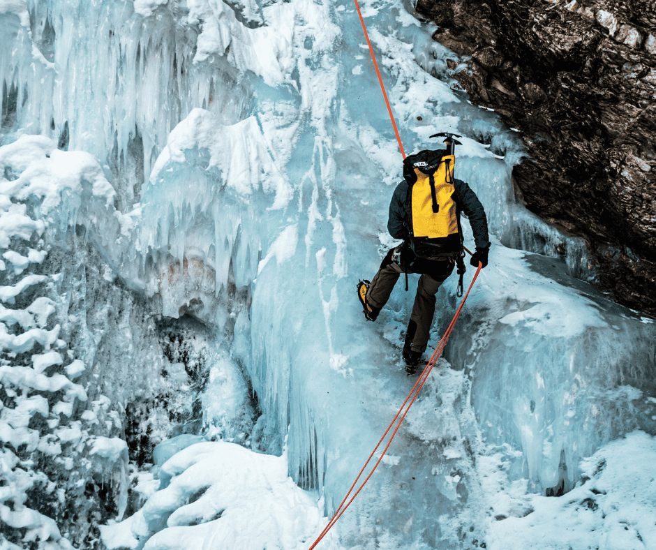 A person ice climbing a frozen waterfall, secured by a rope. Yellow backpack.