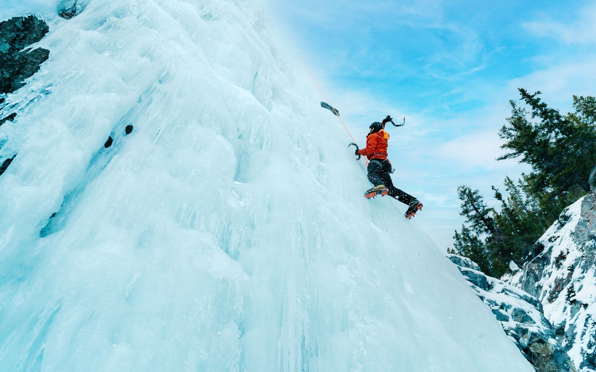 Person ice climbing a frozen waterfall with blue sky background.