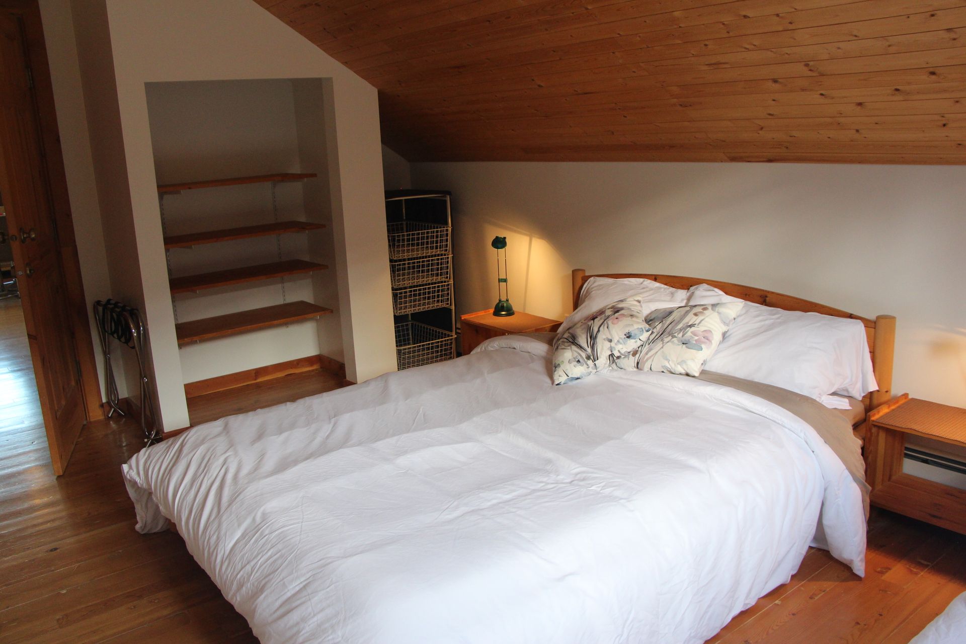 Bedroom with wooden bed, nightstand, built-in shelves, and slanted wooden ceiling.