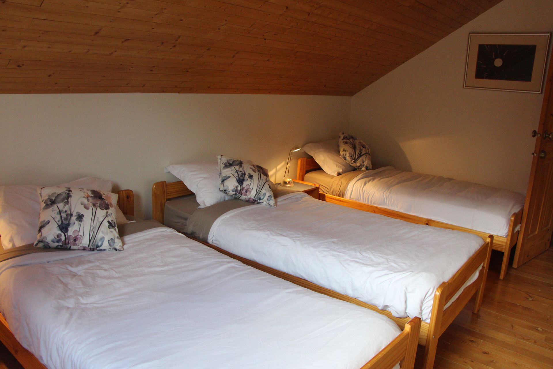 Three single beds in a room with light wood furniture, white bedding, and a sloped ceiling.