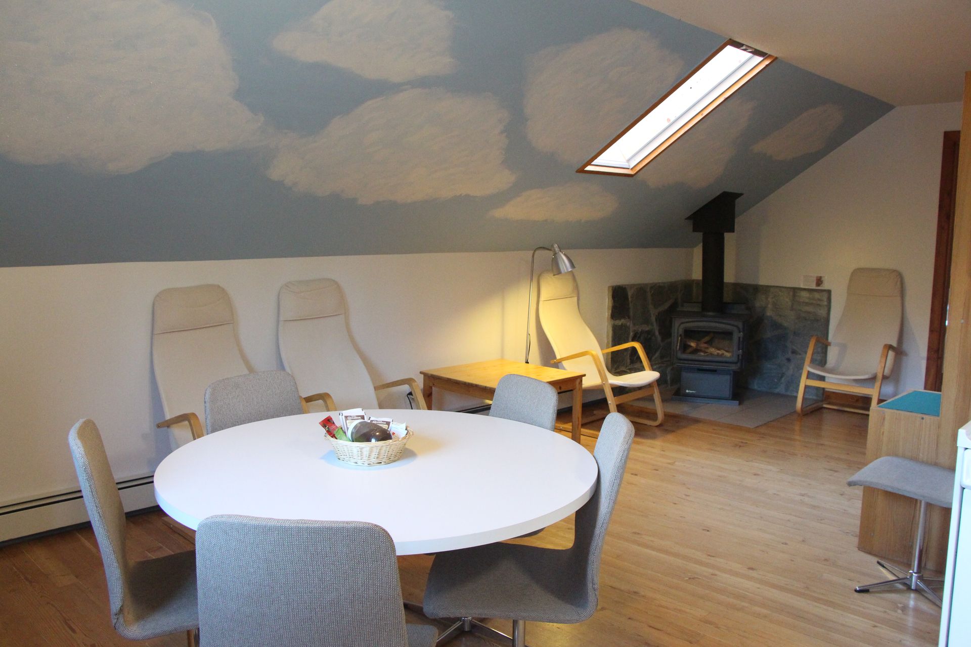 Attic room with round table and chairs, chaise lounges, fireplace, and cloud painted ceiling.