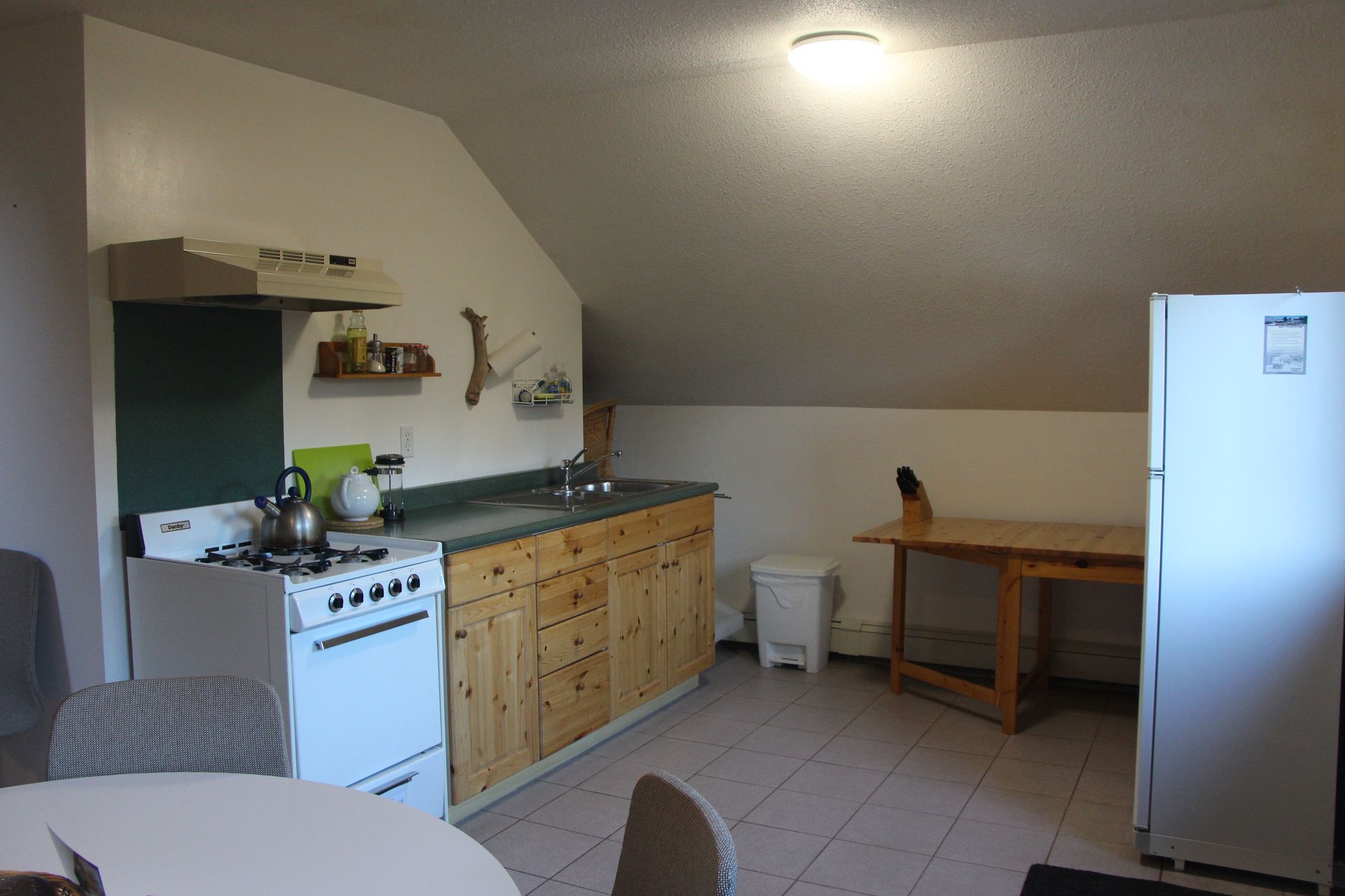 Kitchen with stove, refrigerator, cabinets, and small table under sloped ceiling.