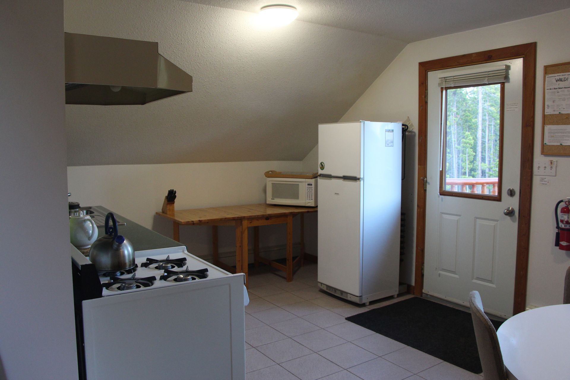 Kitchen with stove, refrigerator, microwave, and table near a doorway to an outdoor deck.