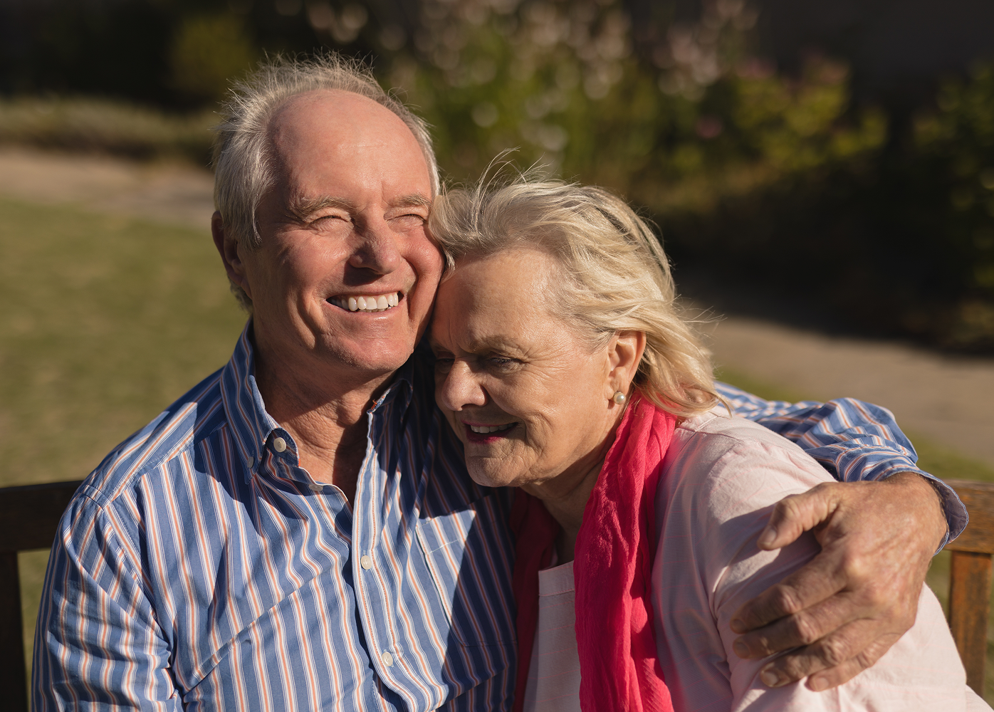 An elderly couple is sitting on a bench and hugging each other.