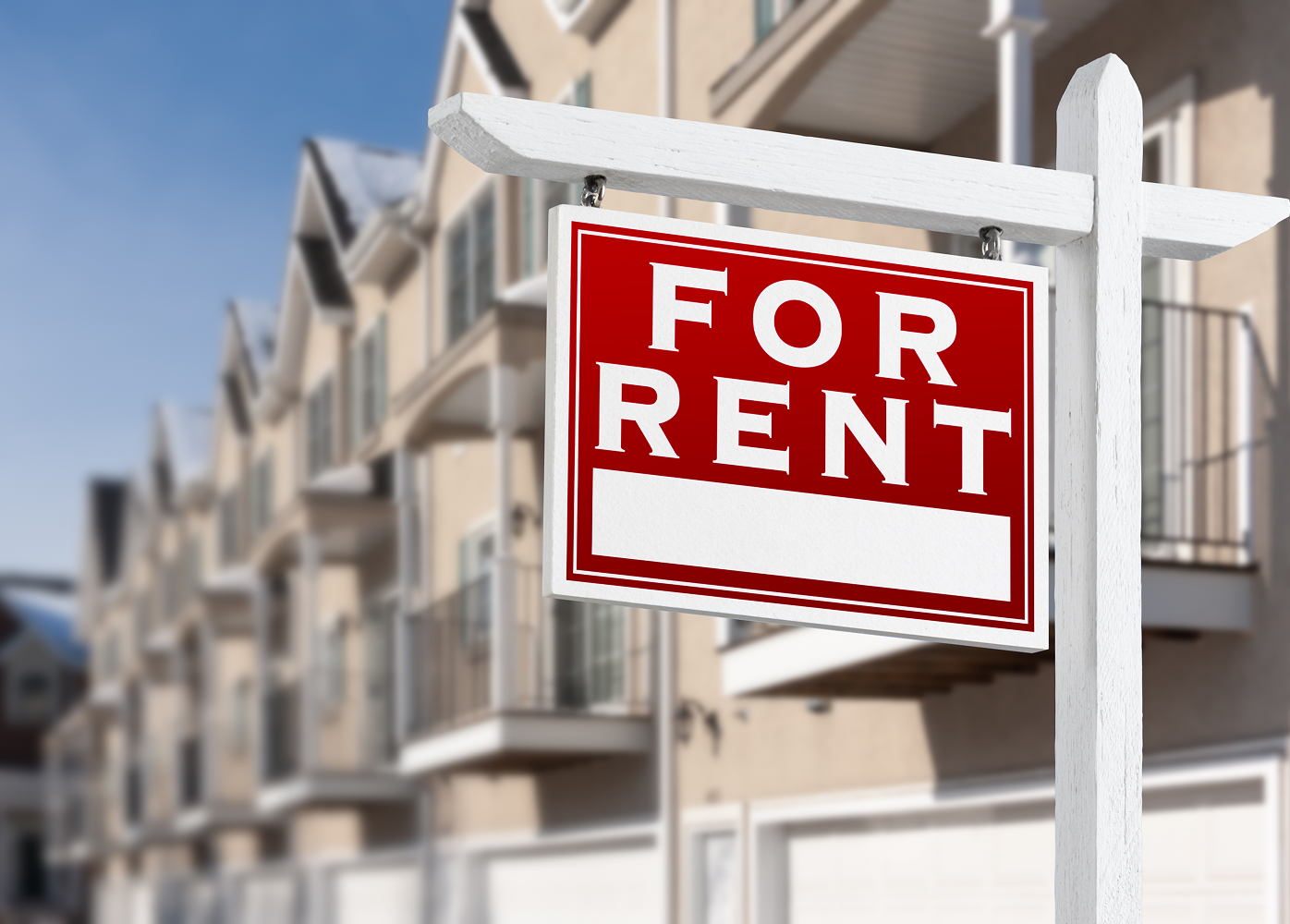 A for rent sign in front of a row of apartment buildings