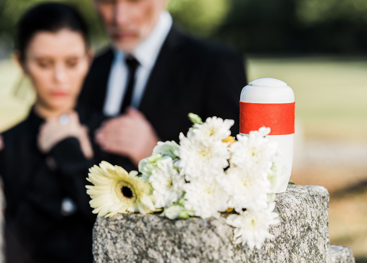 A man and a woman are standing next to a urn with flowers on it.