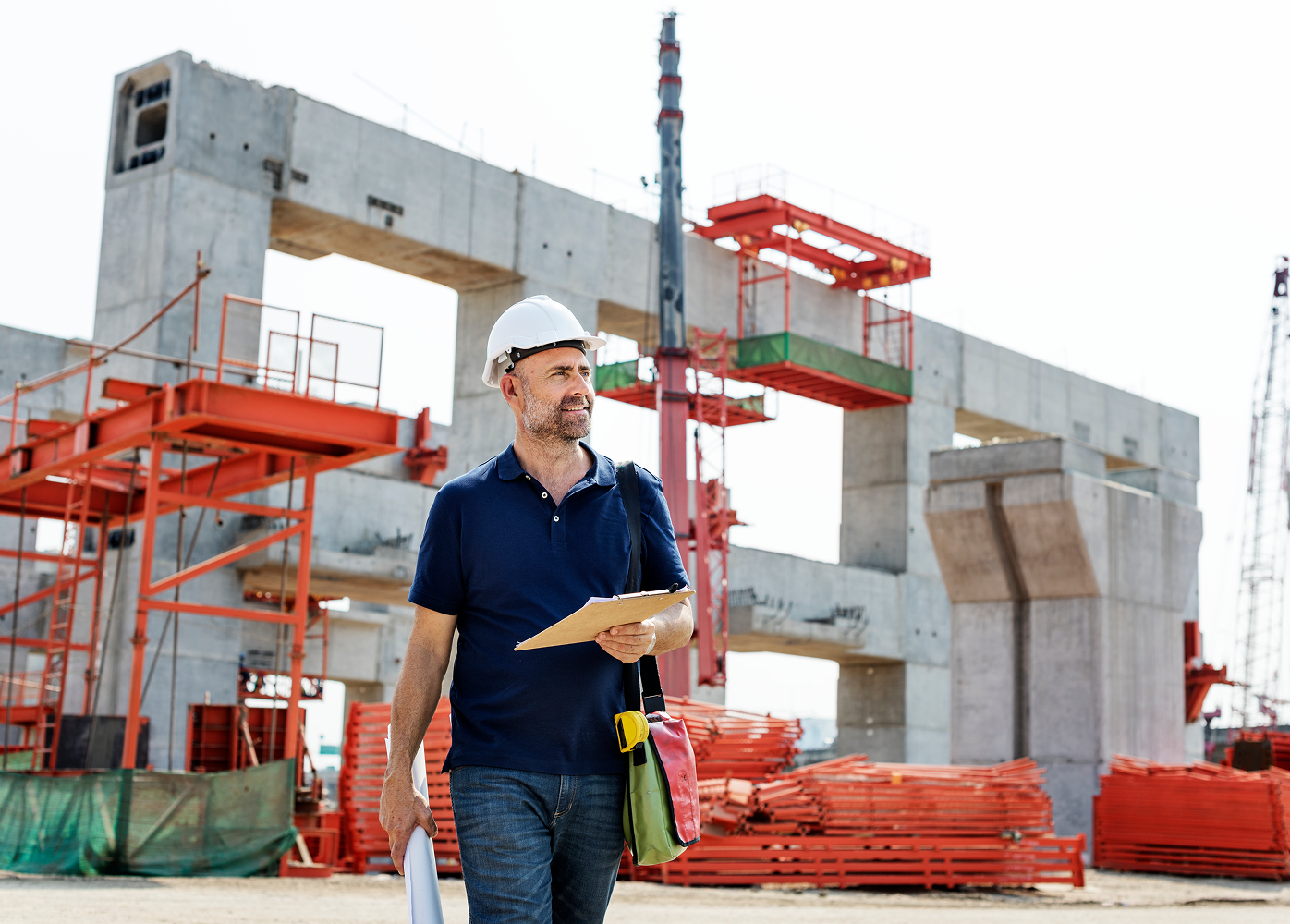 A man is walking on a construction site holding a clipboard.
