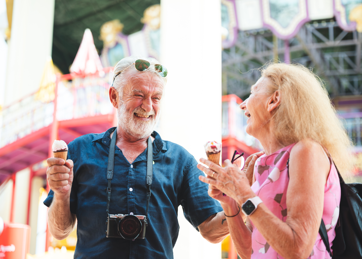 A man and a woman are eating ice cream cones at a carnival.