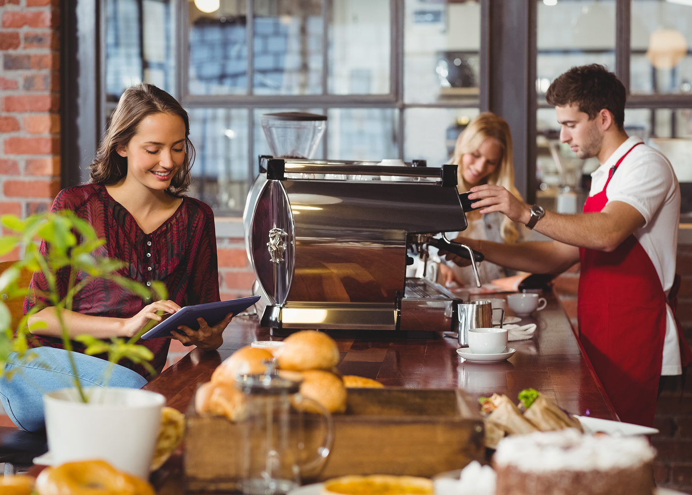 A man is making a cup of coffee while a woman looks at a tablet.