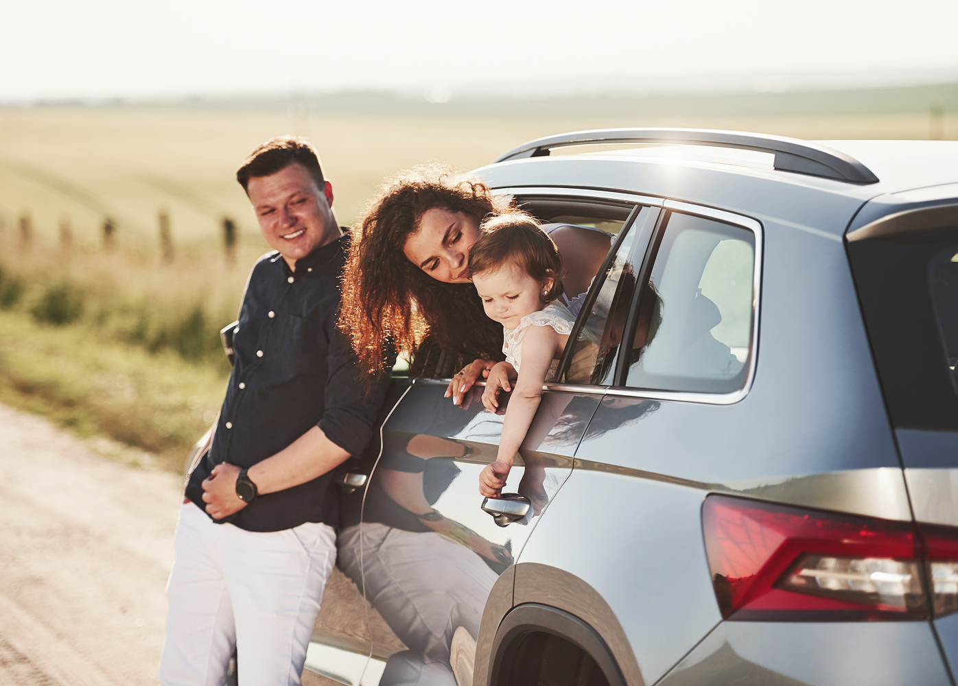 A family is standing next to a car on a dirt road.