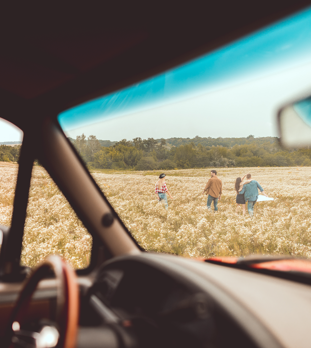 A group of people are walking through a field from the inside of a car
