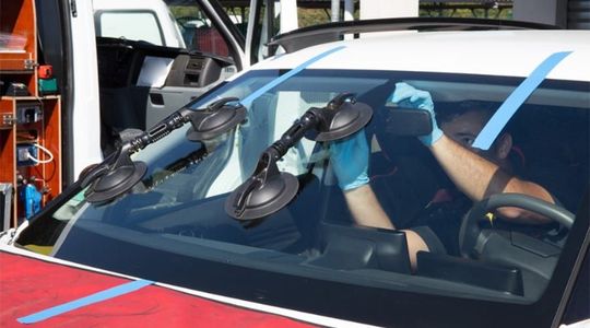 Man replacing front windshield of car with professional tools