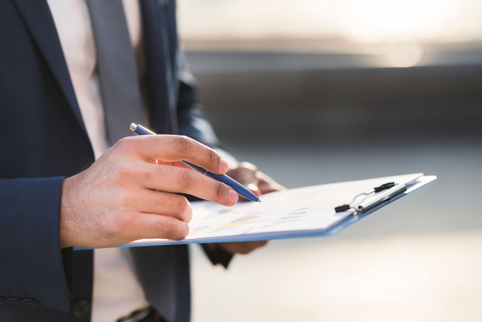 A person in a business suit holding a pen and reviewing documents on a clipboard.