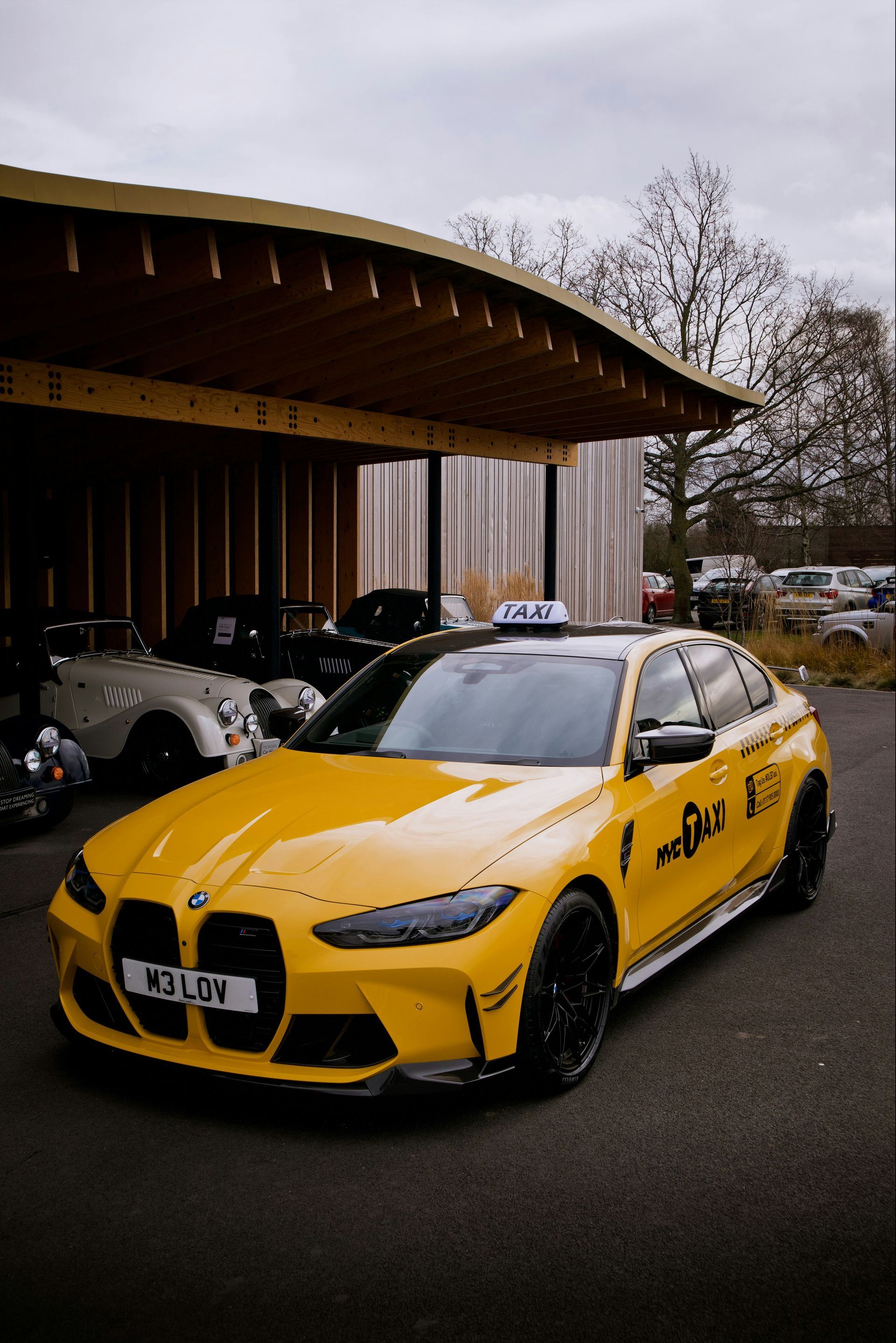 A yellow BMW sedan parked under a wooden structure with a 