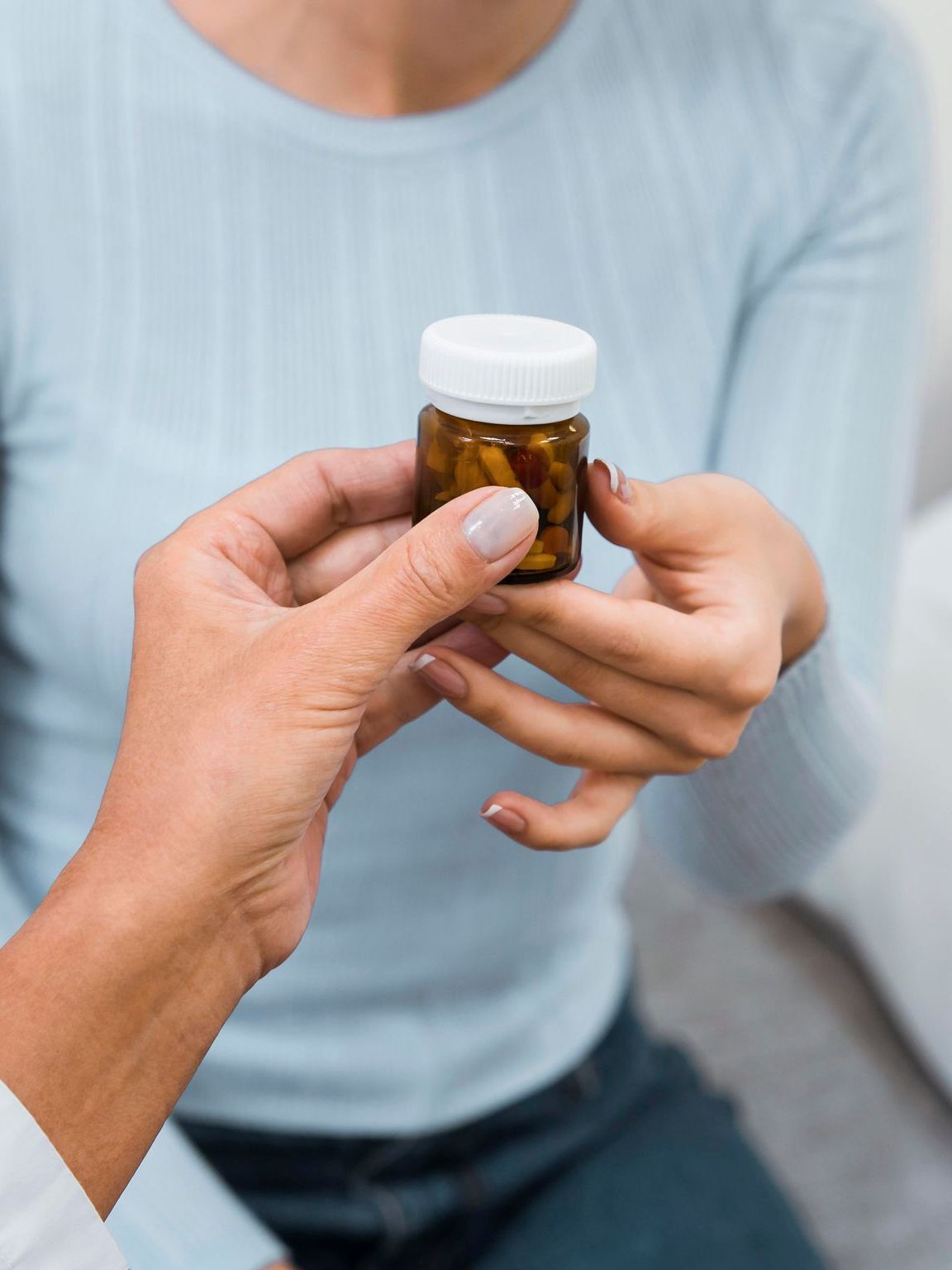 A person hands a small amber pill bottle to another individual.