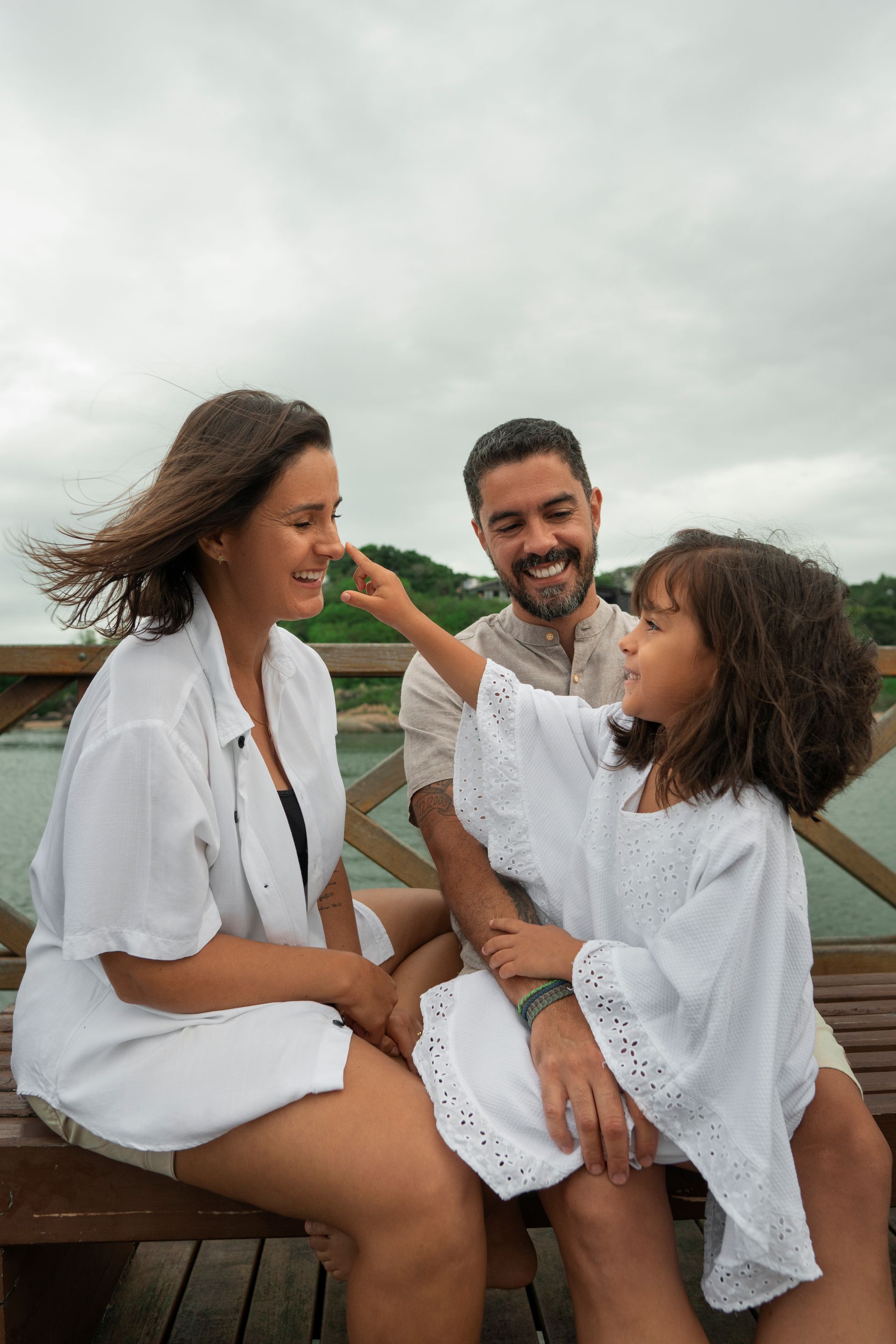 A family sitting on a wooden bench outdoors, with a child playfully touching a smiling person's nose.